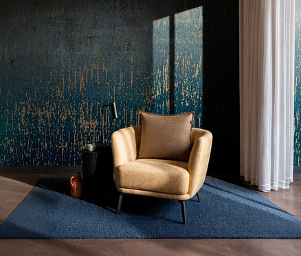 Ein gelber Sessel mit einem braunen SCHÖNER WOHNEN-Kollektion Dekokissen-Bezug »COAST« steht auf einem blauen Teppich vor einer dunkelblauen Wand mit goldenem Muster. Daneben ein schwarzer Beistelltisch mit einer Tasse und einer Lampe.