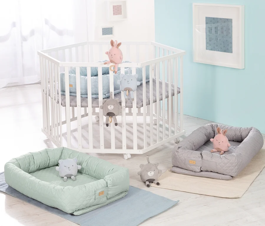 Weißes Kinderbett mit Spielzeug und zwei grüne und graue Babyschalen. Roba 3-in1-Babylounge, grün.