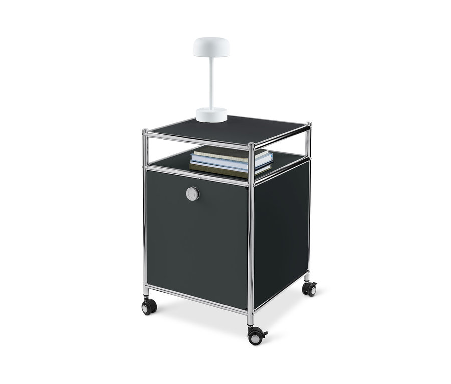 Ein schwarzer Rollcontainer Metall »CN3« mit Klappe, mit Lampe und Büchern darauf.