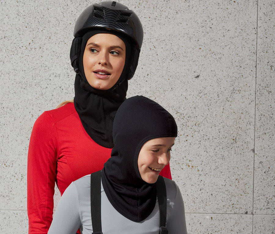 Frau mit Helm und Performance-Sturmhaube steht hinter einem Jungen mit Sturmhaube.