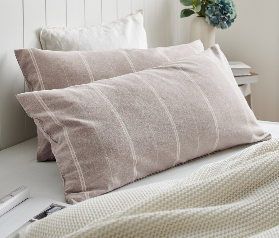 Zwei Edelflanell-Kopfkissenbezüge mit Streifen liegen auf einem Bett neben einer weißen Strickdecke.