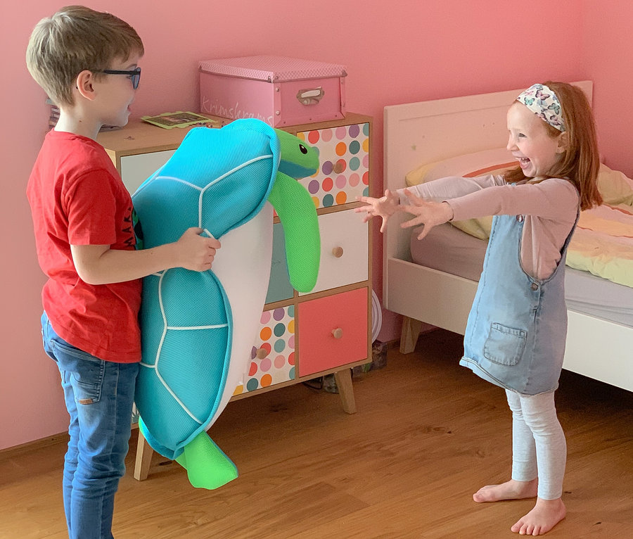 Junge hält Pool Buddy Schildkröte, Mädchen steht mit ausgestreckten Armen da.