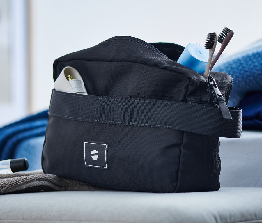 Eine Kulturtasche, ein Handtuch und Kosmetika liegen auf einem Hocker.