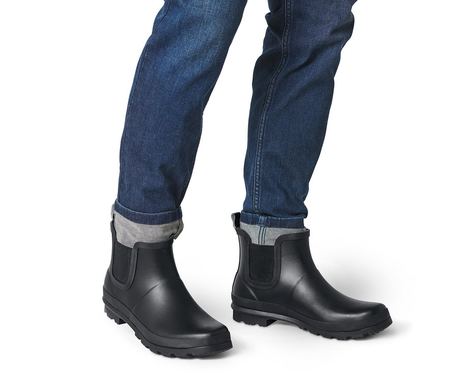 Beine in Jeans und schwarzen Regen-Chelseaboots.