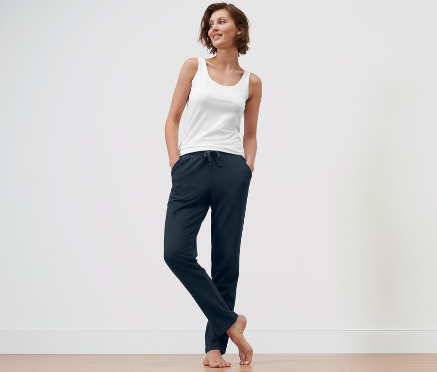 Frau steht mit Händen in den Taschen einer dunkelblauen Loungewear-Hose und einer blauen Loungehose.