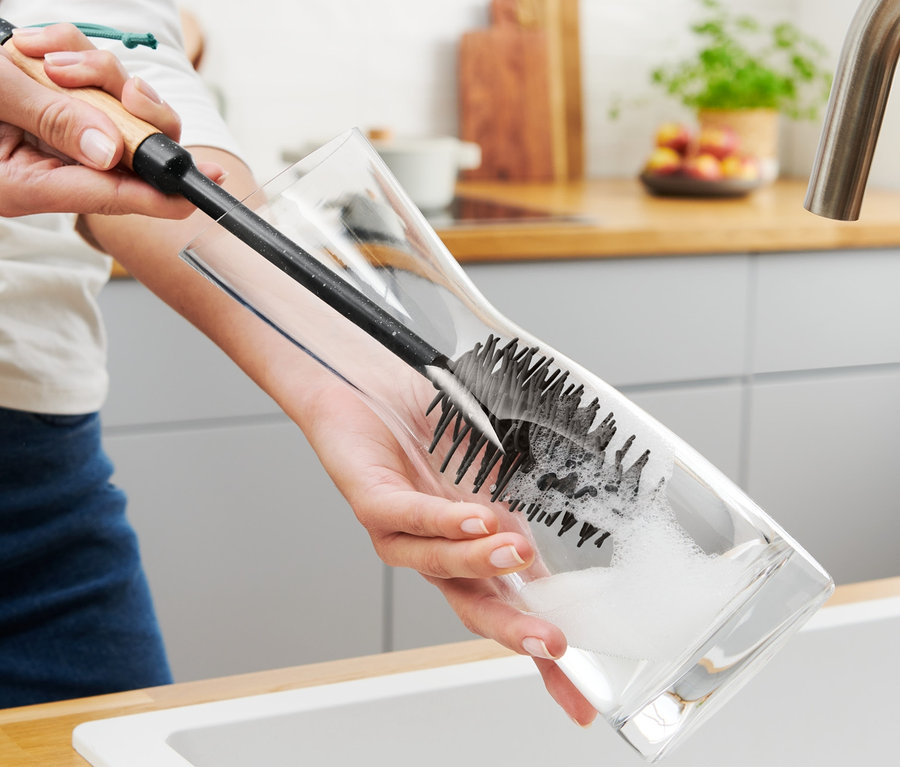 Frau spült ein Glas mit einer Flaschen- und Gläserspülbürste.
