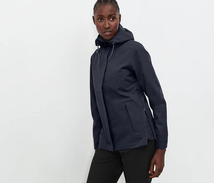 Frau posiert in marineblauer Funktions-Outdoorjacke und schwarzer Hose.