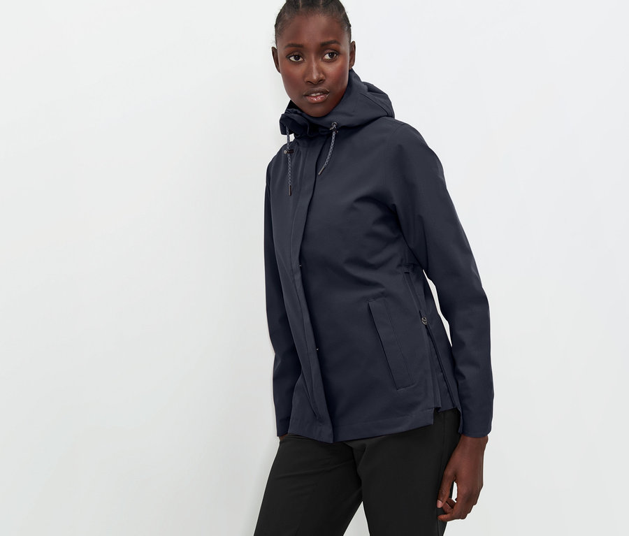 Frau posiert in marineblauer Funktions-Outdoorjacke und schwarzer Hose.