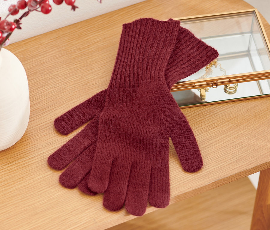 Strickhandschuhe mit Wolle liegen auf einem Holztisch neben einer Vase mit roten Beeren und einem Schmuckkästchen.