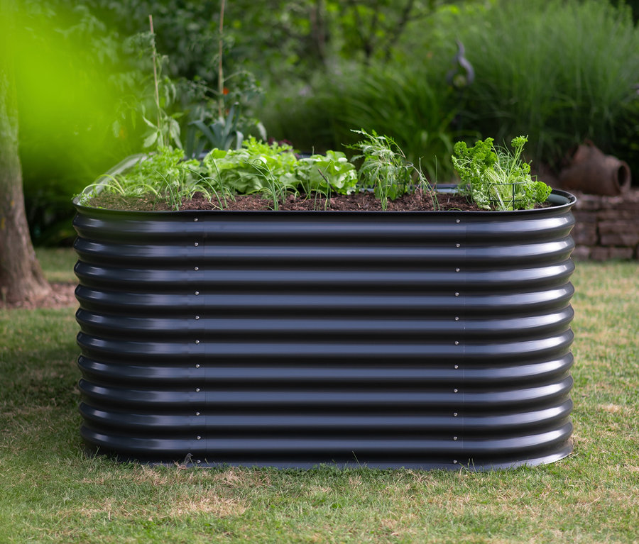 Schwarzes Hochbeet in L-Form auf einer Wiese.
