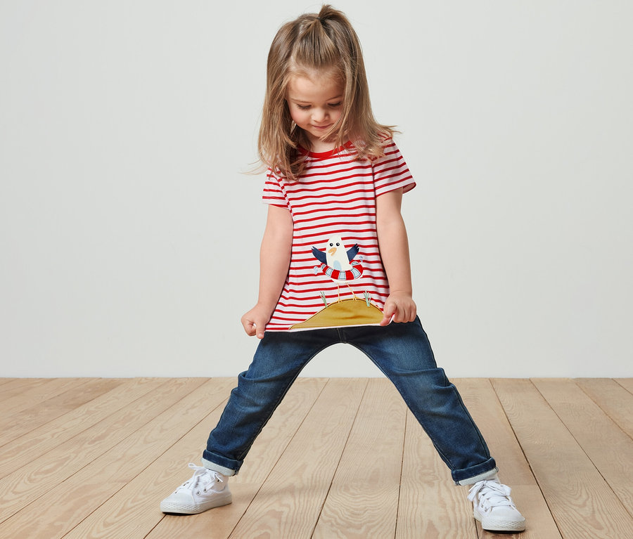 Mädchen steht und hält den Saum ihres rot gestreiften T-Shirts mit Applikation.