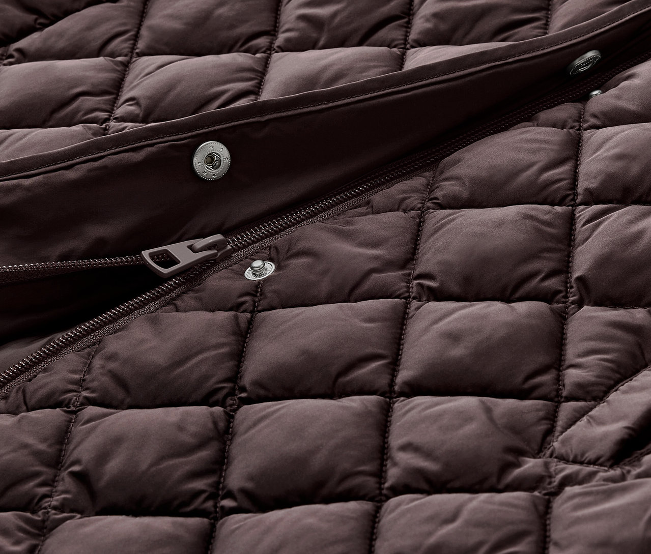 Detailaufnahme einer langen Steppweste mit Kapuze in Dunkelbraun.