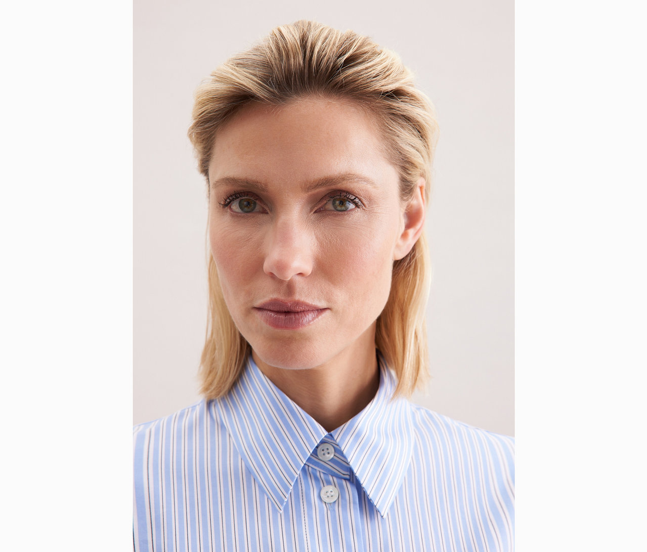 Nahaufnahme einer Frau mit blonden Haaren, die eine blau-weiss gestreifte Seidensticker Oversize-Hemdbluse trägt.