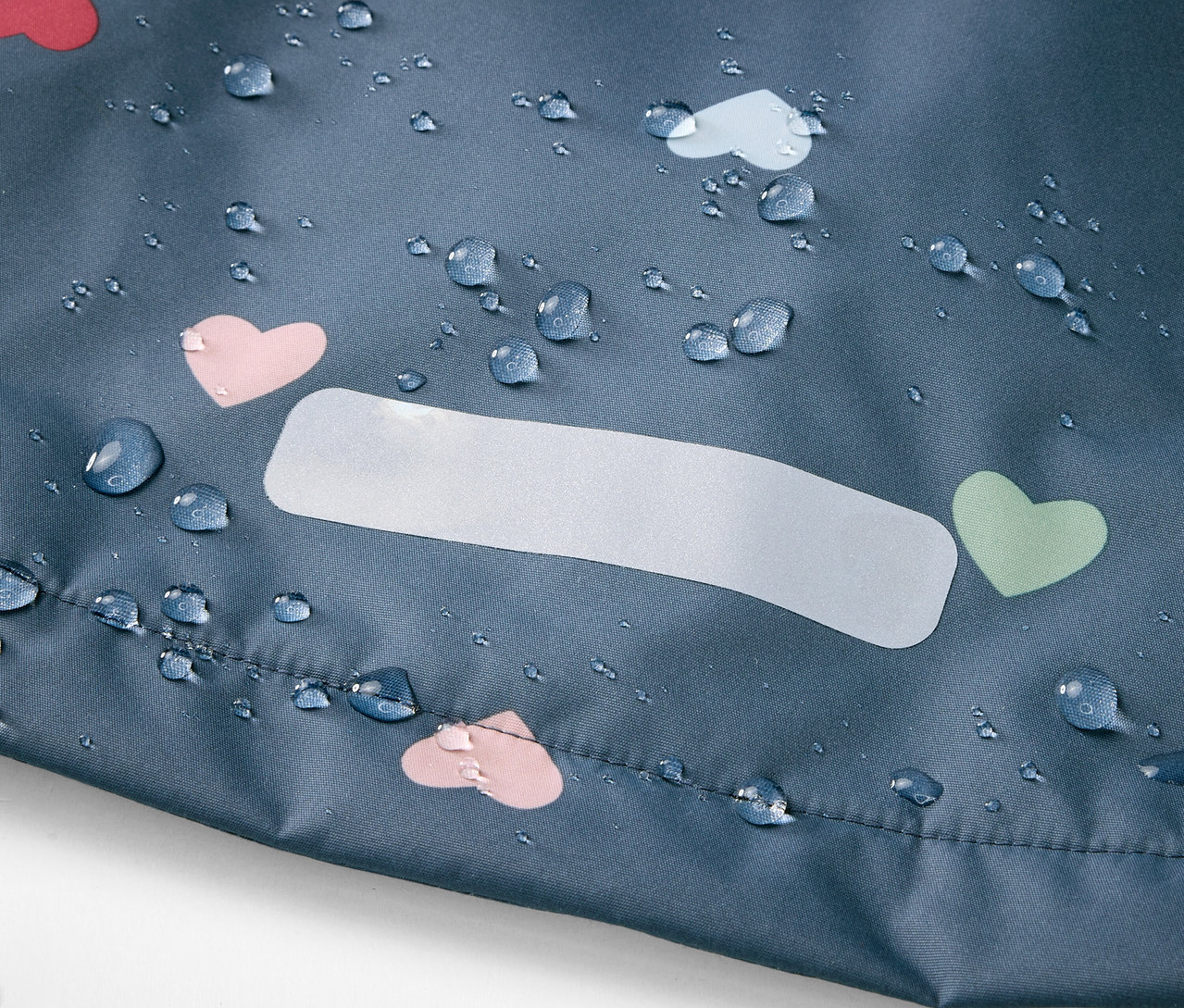 Detailaufnahme einer Kinder-Thermo-Regenjacke mit Herzchenmuster und Wassertropfen.