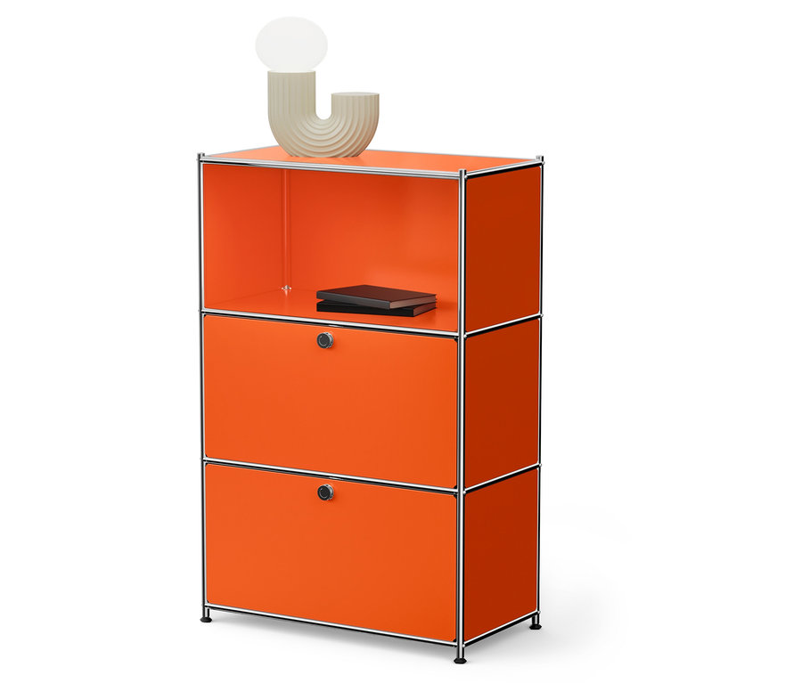 Ein orangefarbenes modulares Schranksystem mit zwei Schubladen und einem offenen Regal, auf dem zwei schwarze Bücher liegen und eine beige Lampe steht.