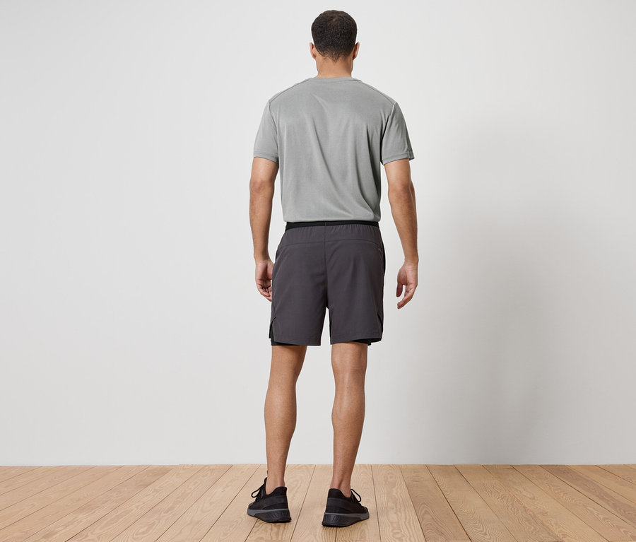 Ein Mann mit dem Rücken zur Kamera trägt ein graues T-Shirt, graue Shorts und schwarze Turnschuhe.