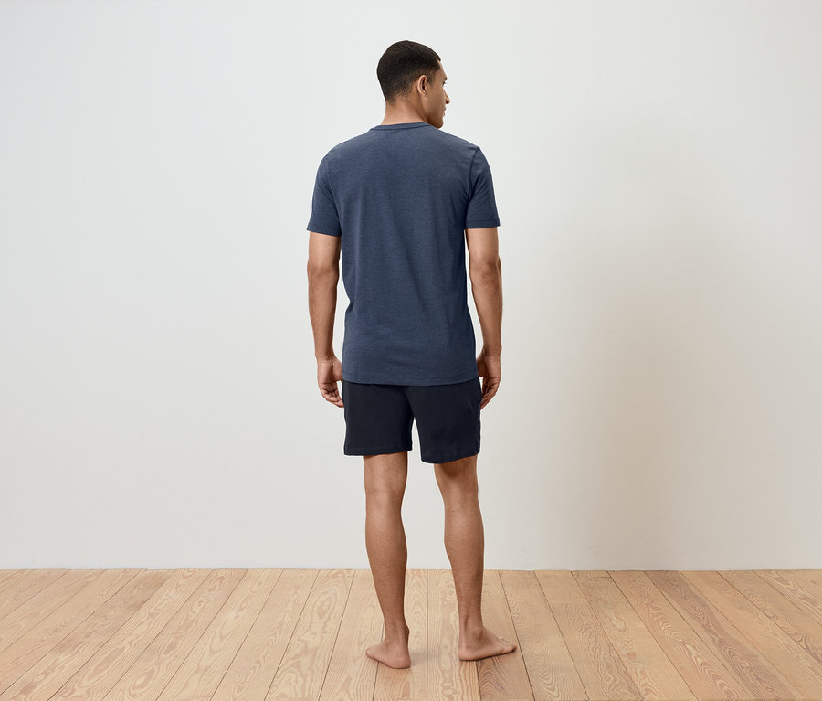 Mann steht mit dem Rücken zur Kamera, trägt ein blaues T-Shirt und schwarze Shorts.