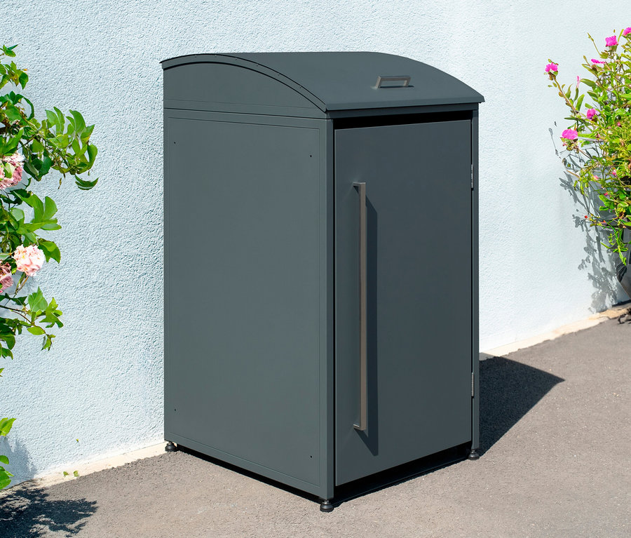 Graue Mülltonnenbox 1er neben Wand und Blumen.