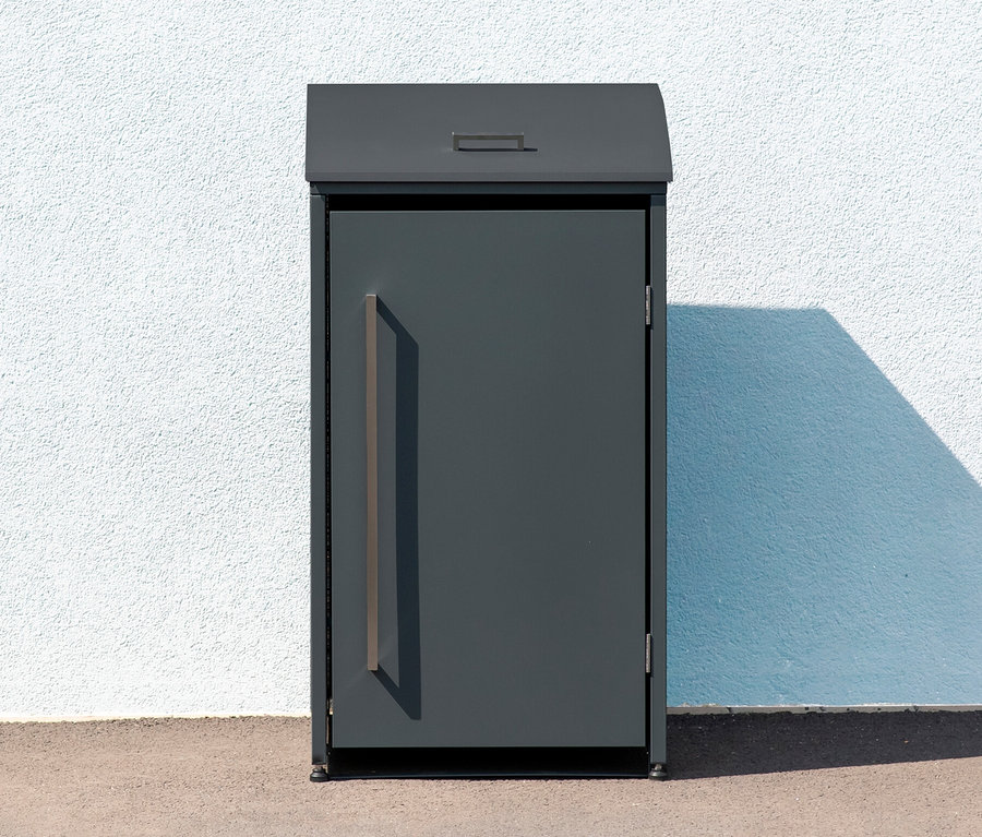 Eine graue Mülltonnenbox, 1er, steht vor einer weißen Wand.