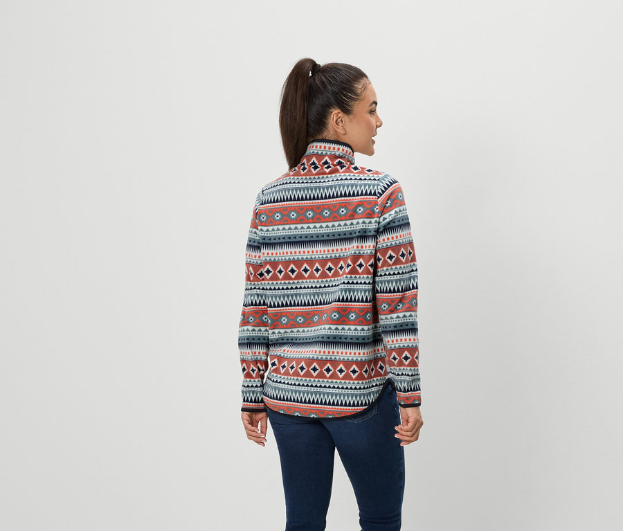 Frau mit braunen Haaren, die zu einem Pferdeschwanz zusammengebunden sind, steht mit dem Rücken zur Kamera und trägt blaue Jeans und eine gemusterte Fleecejacke.