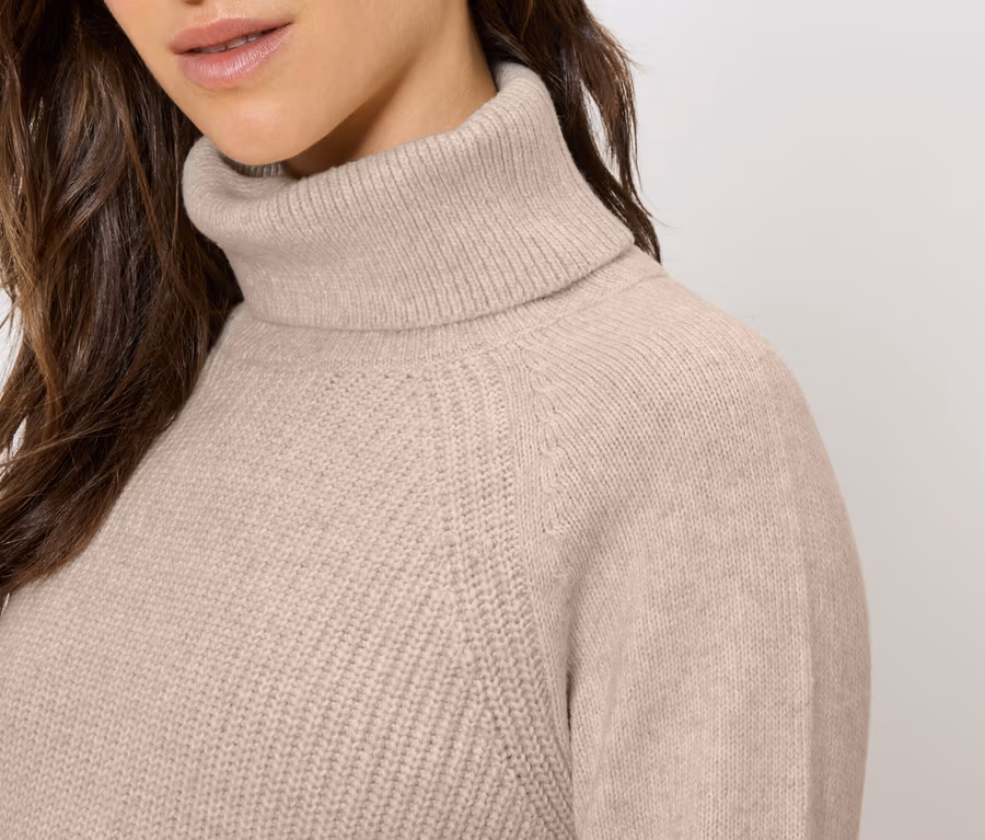 Detailaufnahme einer Frau, die einen beigen Rollkragenpullover trägt.