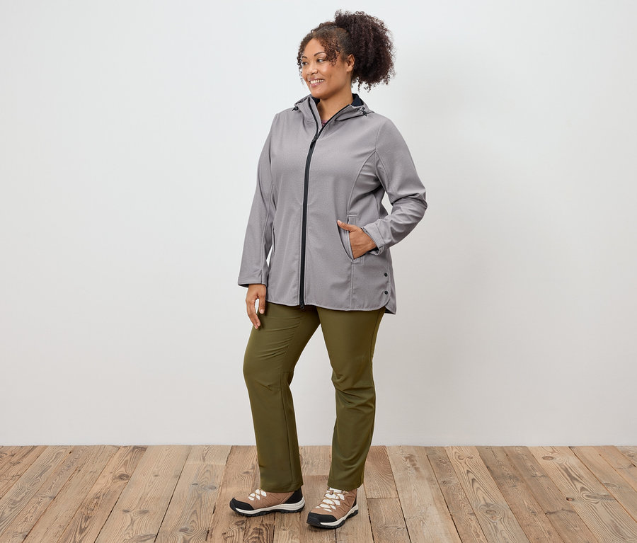 Frau posiert in grauer Jacke, grüner Hose und Sportschuhen.