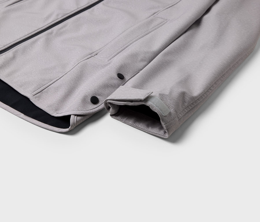 Detailaufnahme einer grauen Jacke mit schwarzem Saum und Druckknopfverschluss.