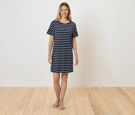 Eine Frau steht auf einem Holzboden und trägt ein gestreiftes T-Shirt-Kleid.