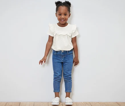 Lächelndes kleines Mädchen posiert in hellem Kinder-T-Shirt und blauen Jeans.