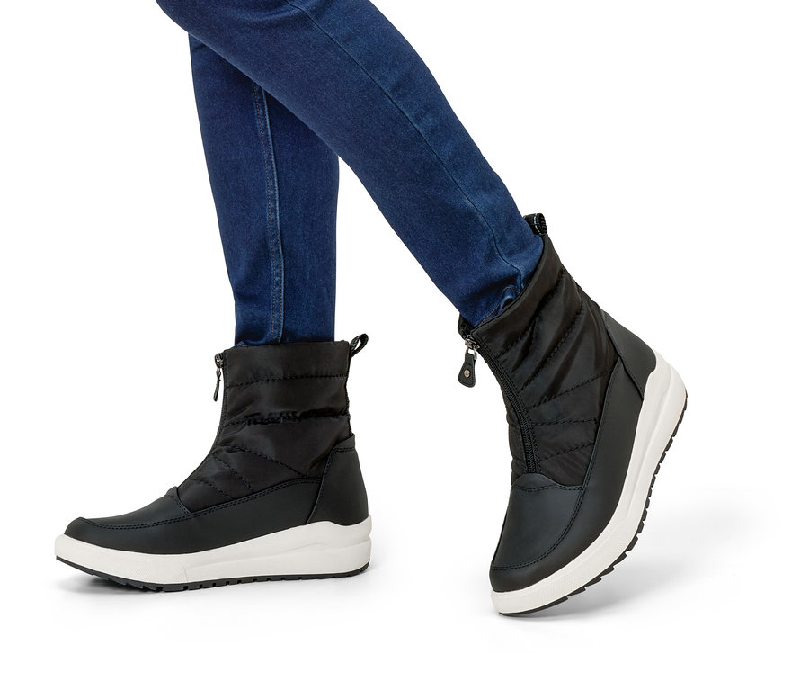 Beine in Jeans und schwarzen Winterstiefeln mit weißen Sohlen.