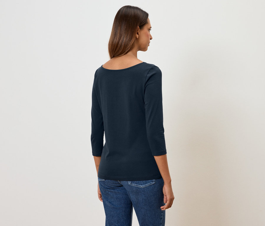 Frau mit dem Rücken zur Kamera trägt ein marineblaues Dreiviertelarmshirt und Jeans.