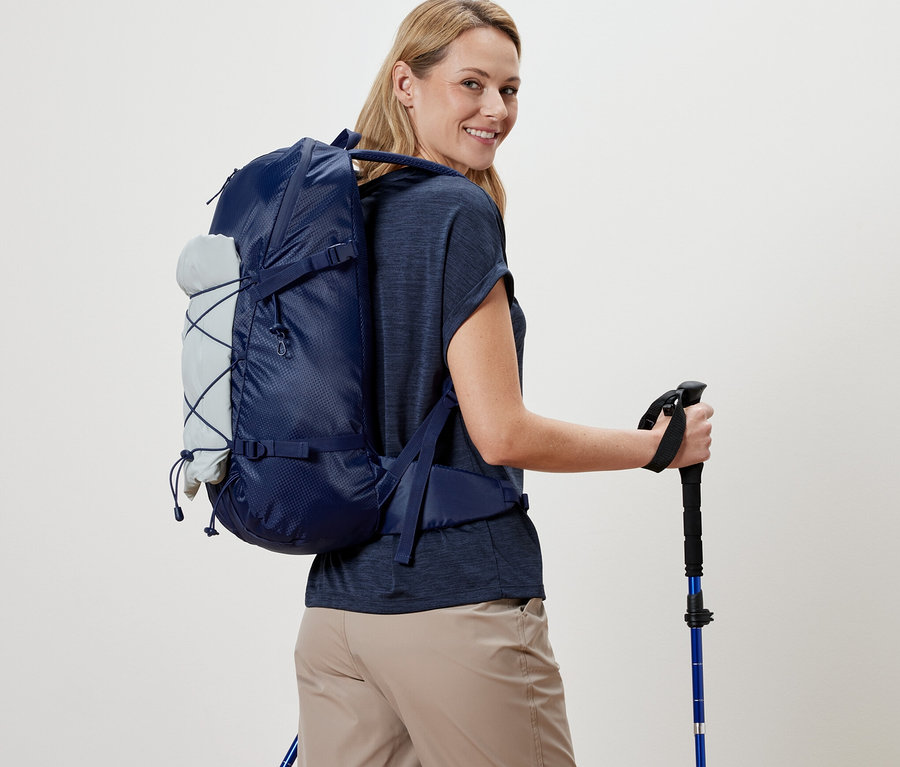 Frau mit Outdoor-Rucksack und Trekkingstöcken blickt über die Schulter.