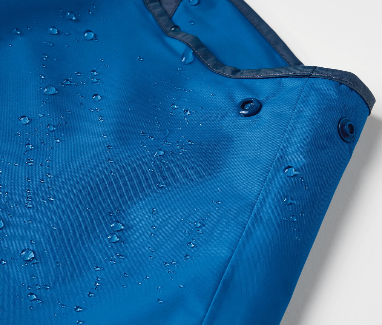 Detailaufnahme einer blauen Kinder-Thermo-Regenhose mit Wassertropfen.