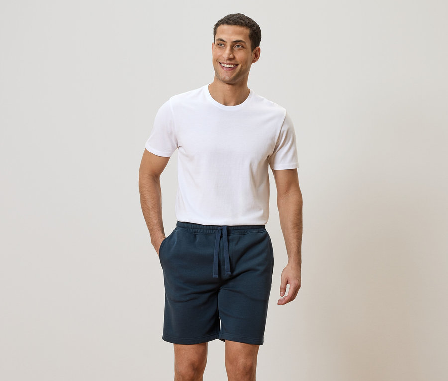 Mann mit weißem T-Shirt und blauen Shorts mit Händen in den Taschen