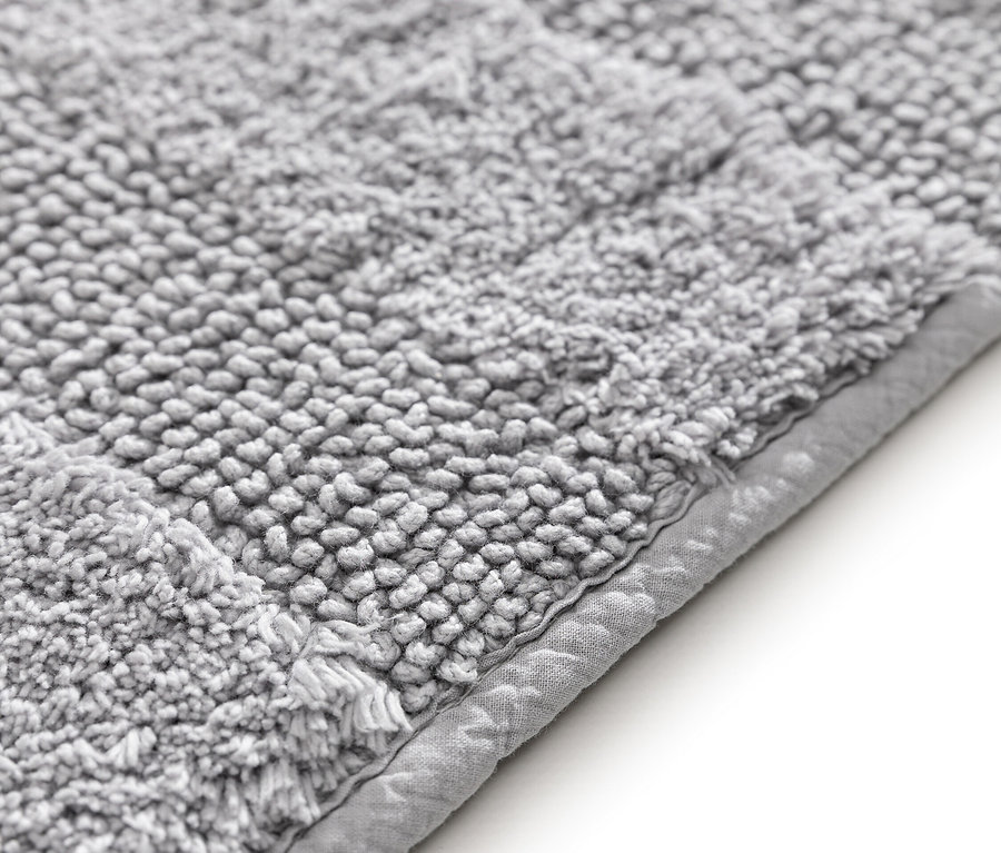 Nahaufnahme einer grauen Badematte mit gewebter Textur und einem schmalen, einfarbigen Rand.