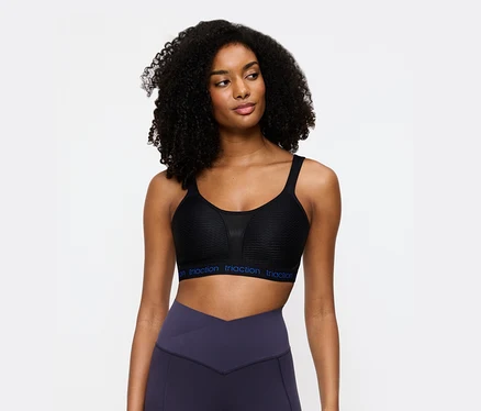 Frau trägt einen schwarzen Triaction Sport-BH und violette Leggings.