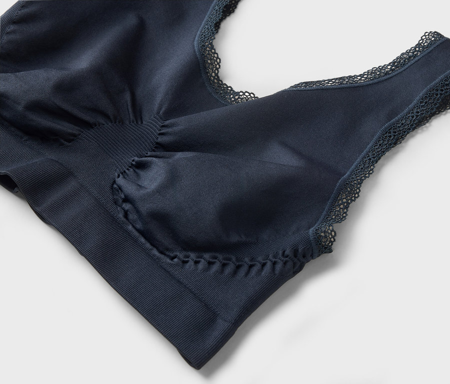 Detailaufnahme eines marineblauen BHs mit Spitzenbesatz auf grauem Hintergrund.