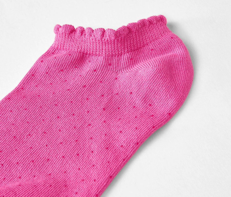 Nahaufnahme eines einzelnen, pinkfarbenen, niedrig geschnittenen Söckchens mit Rüschenrand und kleinen Punkten auf weißem Hintergrund.