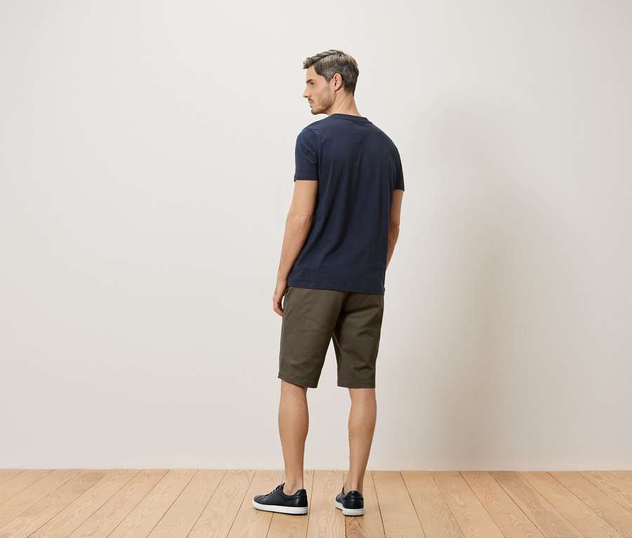 Ein Mann steht mit dem Rücken zur Kamera und trägt ein marineblaues T-Shirt, Khaki-Shorts und marineblaue Schuhe.
