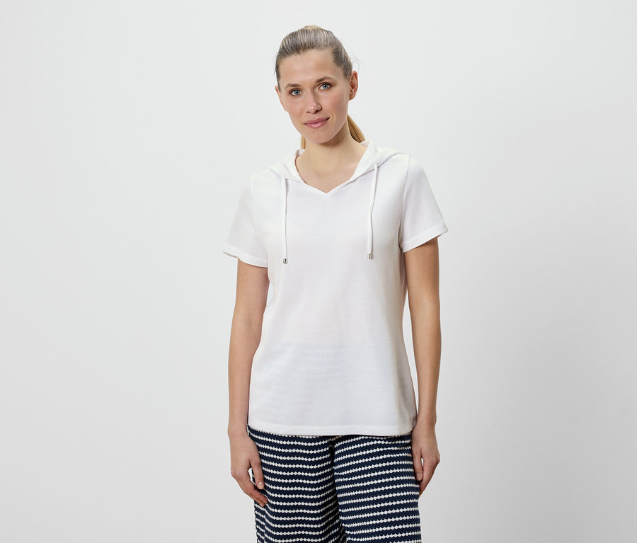 Frau trägt ein weißes Kapuzen-T-Shirt und eine blau-weiß gestreifte Hose.