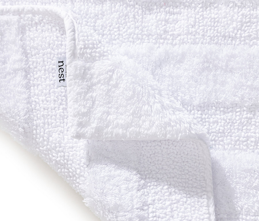 Detailansicht eines weißen, flauschigen Nest-Handtuchs, leicht gefaltet, mit sichtbarem Etikett.