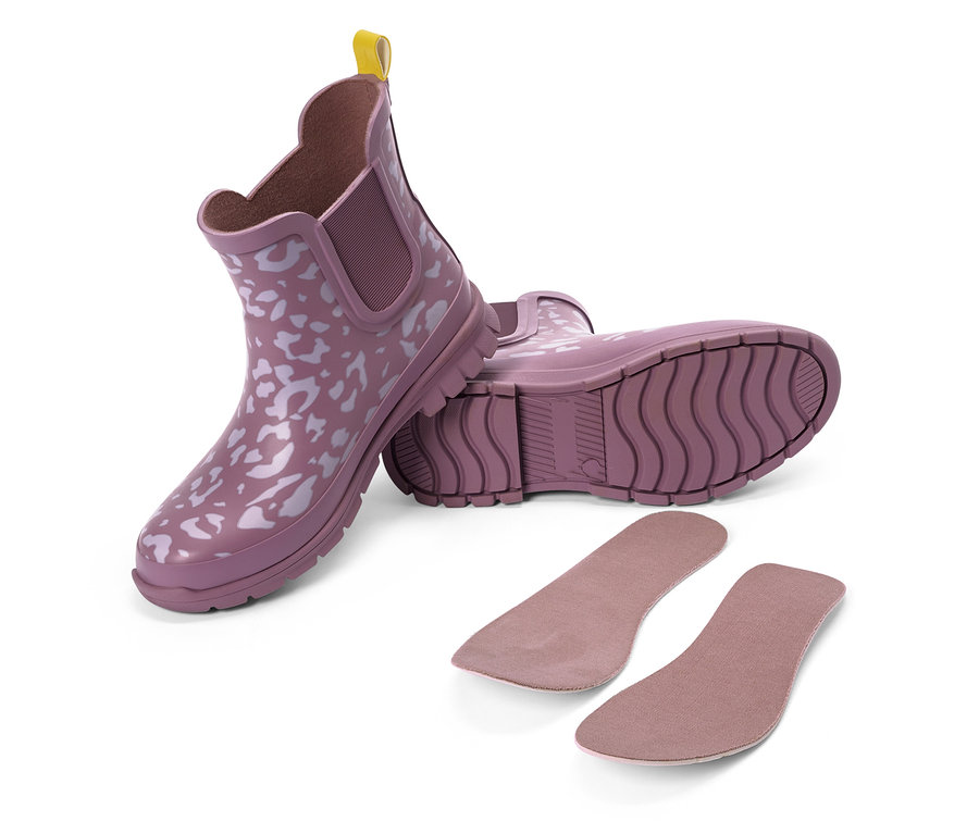 Zwei lila Gummistiefel mit weißem Muster und gelber Lasche, daneben zwei Einlegesohlen.