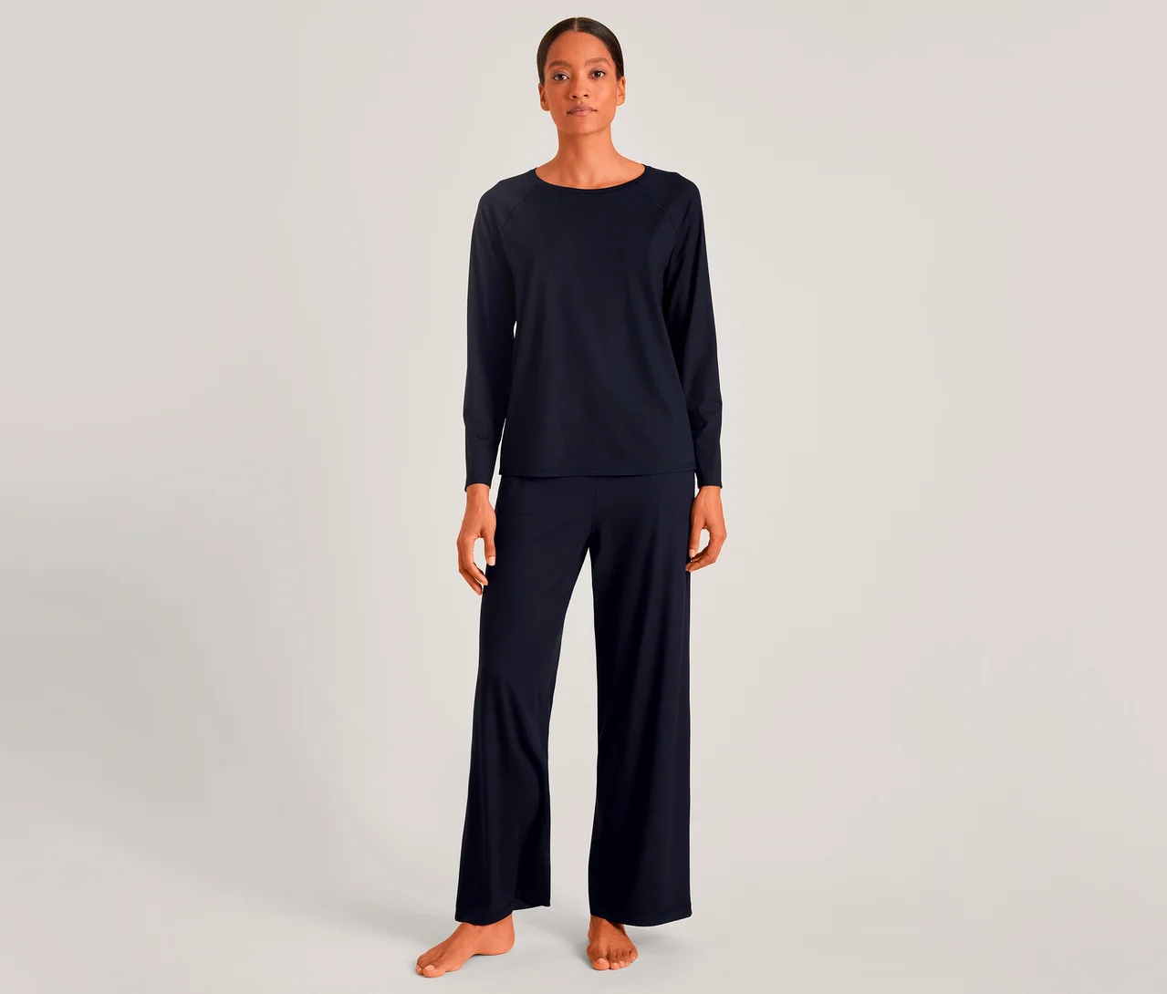 Frau in dunkelblauem Langarmshirt und passender weiter Hose, barfuß stehend.