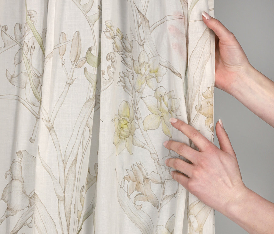 Hände halten einen cremefarbenen SCHÖNER WOHNEN-Kollektion Vorhang »LOVELY« mit zartem Blumenmuster aus hellgelben Blüten und grünen Blättern.