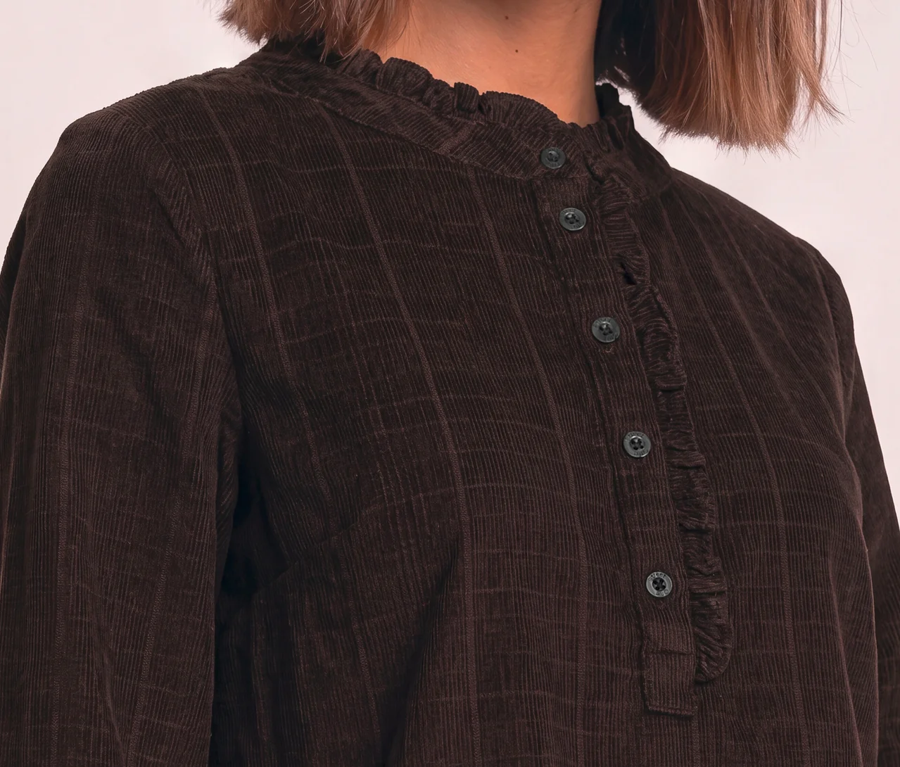 Nahaufnahme einer Person in einer braunen Street One Cordbluse mit Rüschenkragen und Knopfleiste.