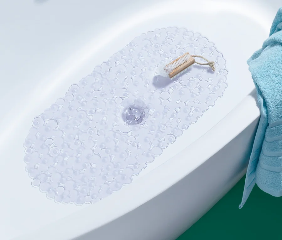 Badewanne mit weißer Badewanneneinlage und einer Bürste auf der Ablage. Ein blaues Handtuch hängt über den Rand der Wanne.