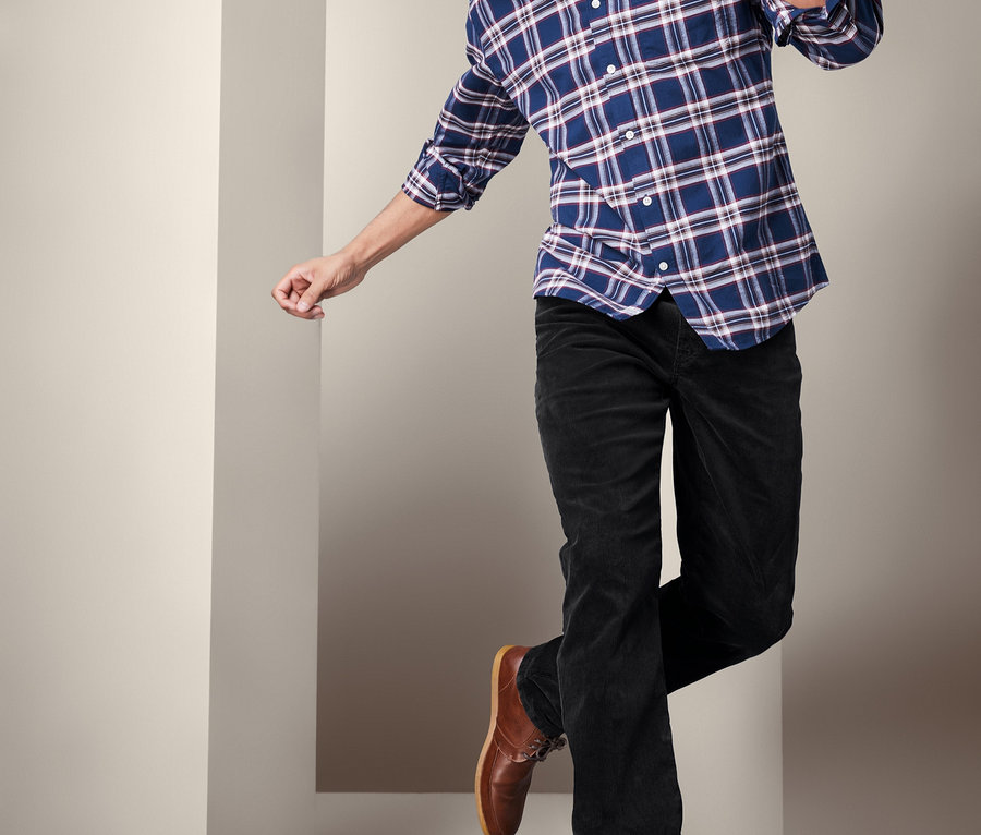 Mann im karierten Hemd und Cordhose springt.