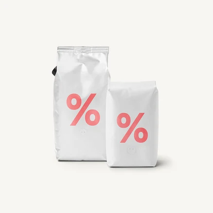 Zwei weiße Kaffeepackungen mit einem rosafarbenen Prozentzeichen-Logo auf hellem Hintergrund.