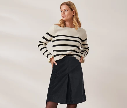 Blonde Frau posiert in einem gestreiften Pullover und einem kurzen Samtrock.