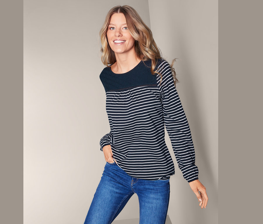 Frau posiert in blau gestreiftem Blusenshirt mit Stickerei und blauen Jeans.